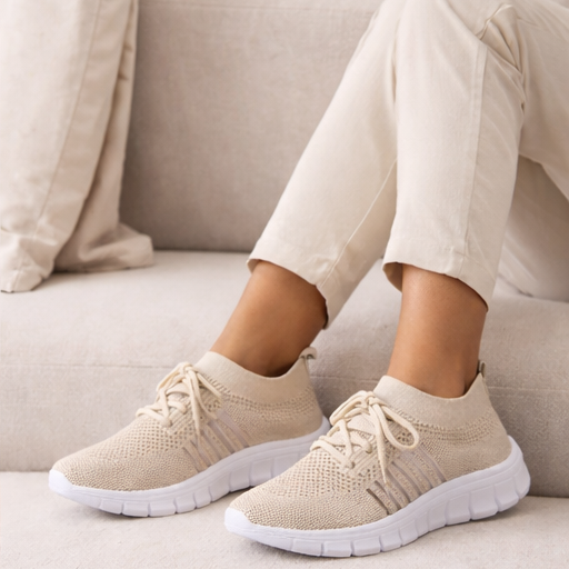 Beige sneakers worn by a person sitting on a light-colored couch.